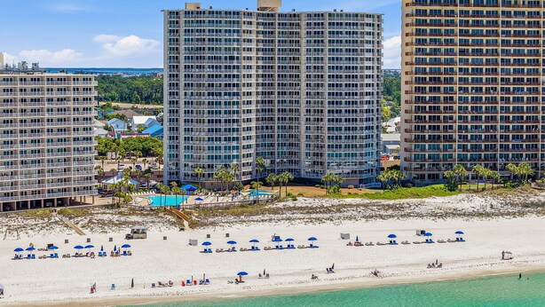 A beachfront hotel with multiple high-rise buildings, a sandy beach with umbrellas, and a clear view of the ocean. - D302 Relax on the Gulf – Beachfront 2BR/2BA with Incredible Views (Panama City Beach)