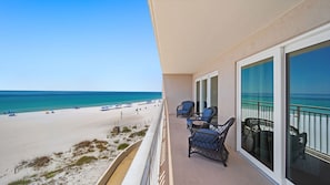 A balcony with wicker chairs, a view of the beach, and a clear sky.
