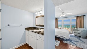 A bedroom with a bed, a bathroom with a sink, and a view of the beach. - D302 Relax on the Gulf – Beachfront 2BR/2BA with Incredible Views (Panama City Beach)