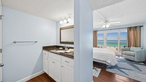 Une chambre avec un lit, une salle de bain avec un lavabo et un miroir, et un balcon avec vue sur l’océan.