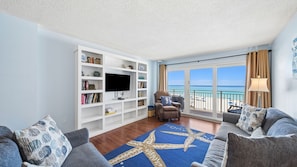 A living room with a large bookshelf, a flat-screen TV, a leather armchair, a sofa, and a starfish-patterned rug.