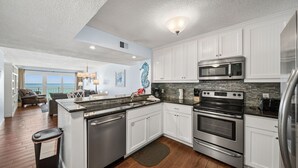 A modern kitchen with white cabinets, stainless steel appliances, and a view to the outside. - D302 Relax on the Gulf – Beachfront 2BR/2BA with Incredible Views (Panama City Beach)
