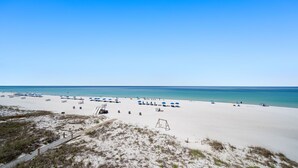 A beach with white sand, clear blue water, and a few umbrellas. - D302 Relax on the Gulf – Beachfront 2BR/2BA with Incredible Views (Panama City Beach)