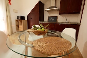 A modern kitchen with a glass dining table, wooden woven placemats, and a fruit bowl. - Hacienda Laguna Seca - Apart. Jazmin (Cadiz)