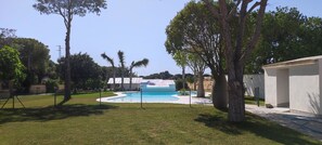 A swimming pool surrounded by a fenced yard with trees and a building in the background. - Hacienda Laguna Seca - Apart. Jazmin (Cadiz)