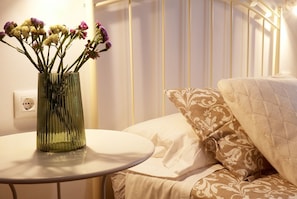 A bedroom with a bed, a bedside table with a vase of flowers, and a white wall with a power outlet. - Hacienda Laguna Seca - Apart. Jazmin (Cadiz)