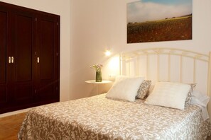 Ein Schlafzimmer mit einem Bett, einem Nachttisch, einer Vase mit Blumen und einem Bild an der Wand.