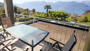 A balcony with a glass table and chairs, overlooking a mountainous landscape and a body of water. - Euroville by Interhome (Luino)