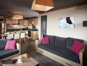 A modern living room with a grey sofa, a dining table with chairs, and a kitchen area in the background.