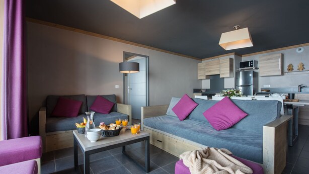 Uma sala de estar moderna com um sofá, uma mesa de centro e um espaço de refeições, com uma cozinha ao fundo.