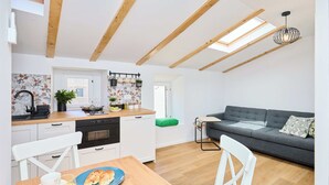 A compact kitchen with wooden beams, a dining area with a table and chairs, and a grey sofa in a living area. - Hedera Estate, Hedera Studio 7 (Dubrovnik)