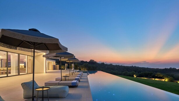 An infinity pool with lounge chairs and umbrellas, a modern building with large windows, and a view of the landscape. - Gavras Exclusive Villa II, Pool & Heated Whirlpool, SeaViews (9HFX+3FH Arkadi, Greece)