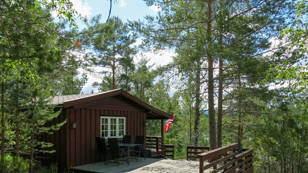 Una cabaña con terraza, una bandera y entorno forestal natural.