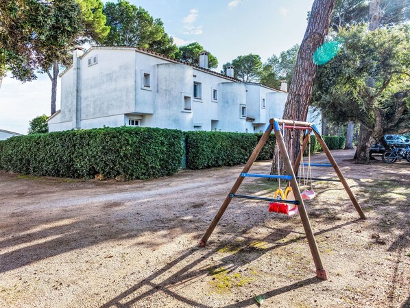 A swing set in a park area with a building in the background. - Trebol Blanco by Interhome (Pals)