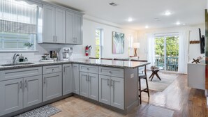 A modern kitchen with grey cabinets, a granite countertop, and a large island. There is a dining area with a table and chairs, and a view of the outdoors through large windows. - 3 BED/2 BATH<br>Free parking space<br>Near Rutgers University, Newark Penn Station, EWR airport, Prudential Center, MetLife Stadium, and more.<br>Fully equipped kitchen<br>Professionally styled (Newark)