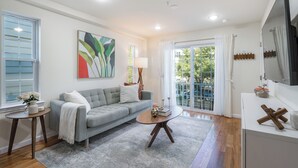 A modern living room with a grey sofa, a round coffee table, and a large window with curtains. - 3 BED/2 BATH<br>Free parking space<br>Near Rutgers University, Newark Penn Station, EWR airport, Prudential Center, MetLife Stadium, and more.<br>Fully equipped kitchen<br>Professionally styled (Newark)