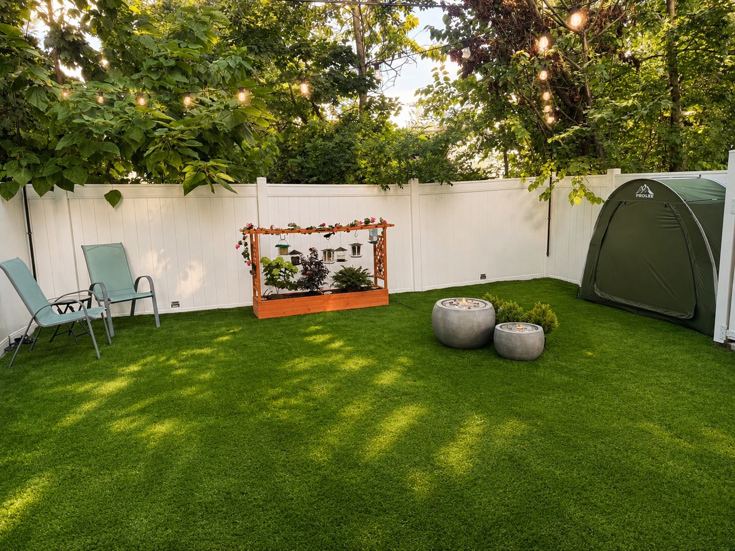 A backyard with artificial grass, a wooden pergola with hanging lights, a tent, and two chairs.