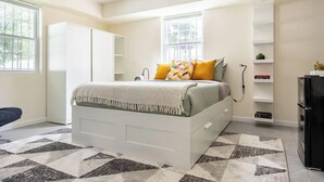 Un dormitorio con cama, escritorio, silla, armario y estante empotrado con libros y una planta.