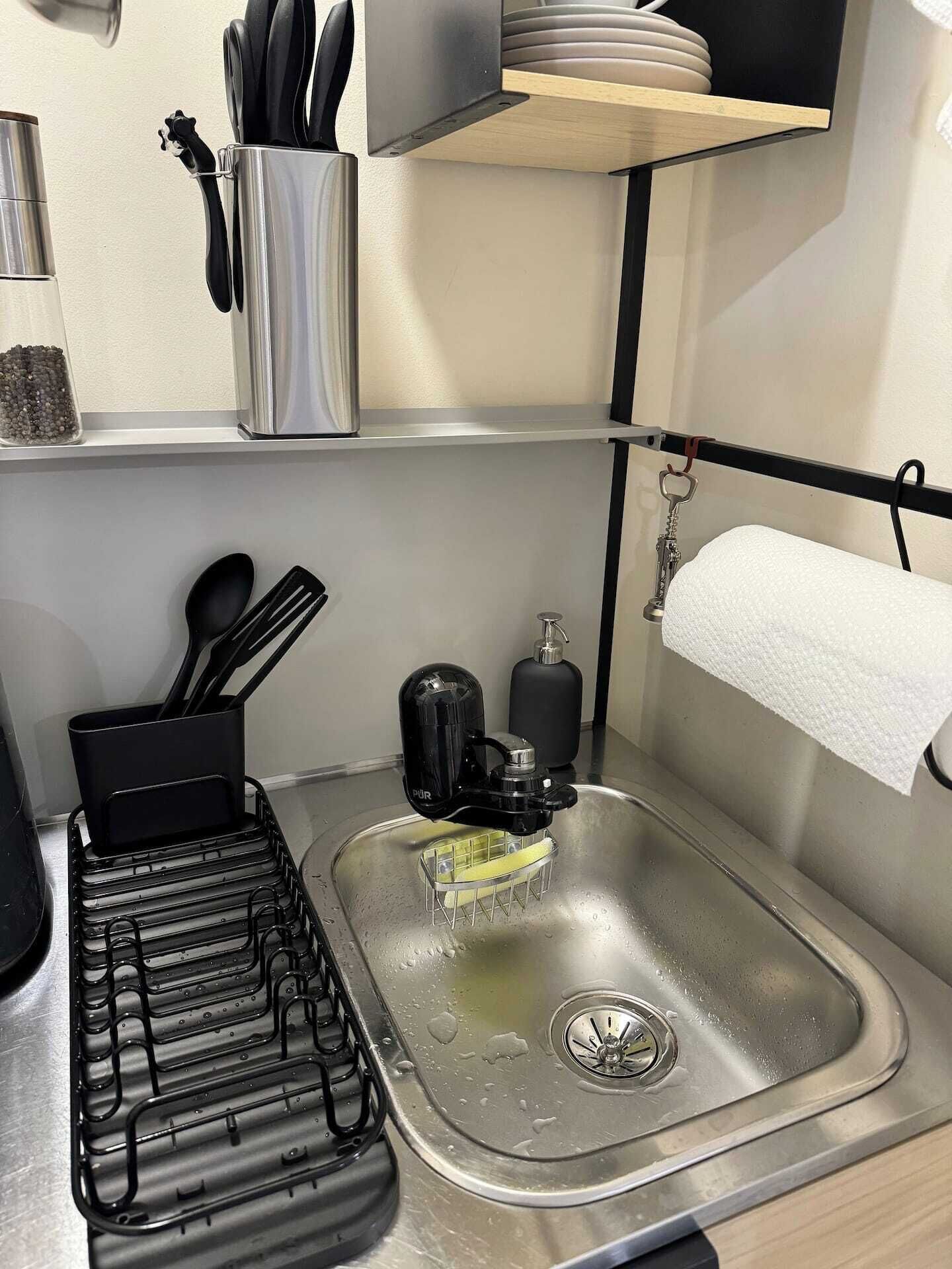 Una cocina compacta con un lavamanos de acero inoxidable, un escurreplatos y un dispensador de jabón.