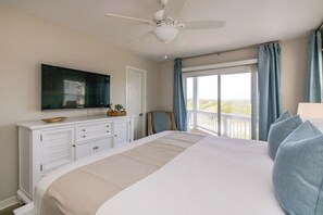 A bedroom with a bed, a ceiling fan, a TV, a dresser, and a view of the outdoors.