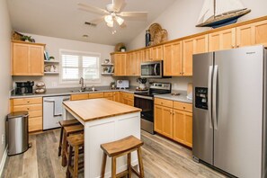 A modern kitchen with wooden cabinets, stainless steel appliances, a central island with stools, and a ceiling fan.