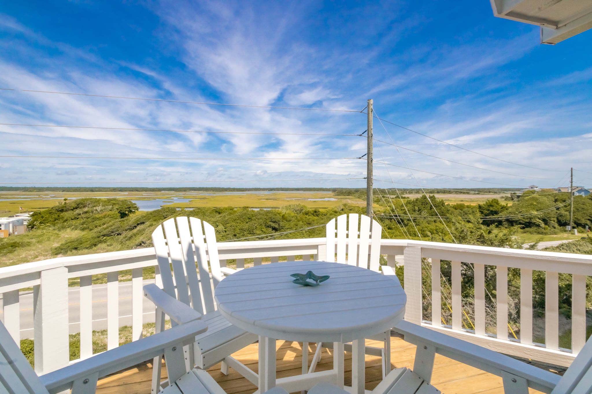 A deck with a table and two chairs, overlooking a landscape with open fields and a body of water.