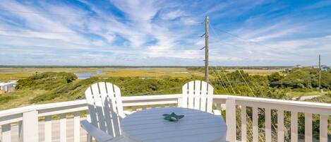 A deck with a table and two chairs, overlooking a landscape with open fields and a body of water.