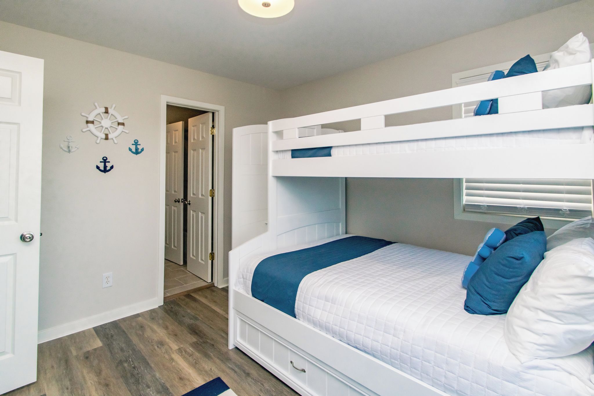 Una cama litera con una manta y almohadas azules, una puerta blanca y un pasillo con suelo de madera.