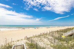 A beach with a wooden walkway leading to the shore, sandy beach, and ocean.