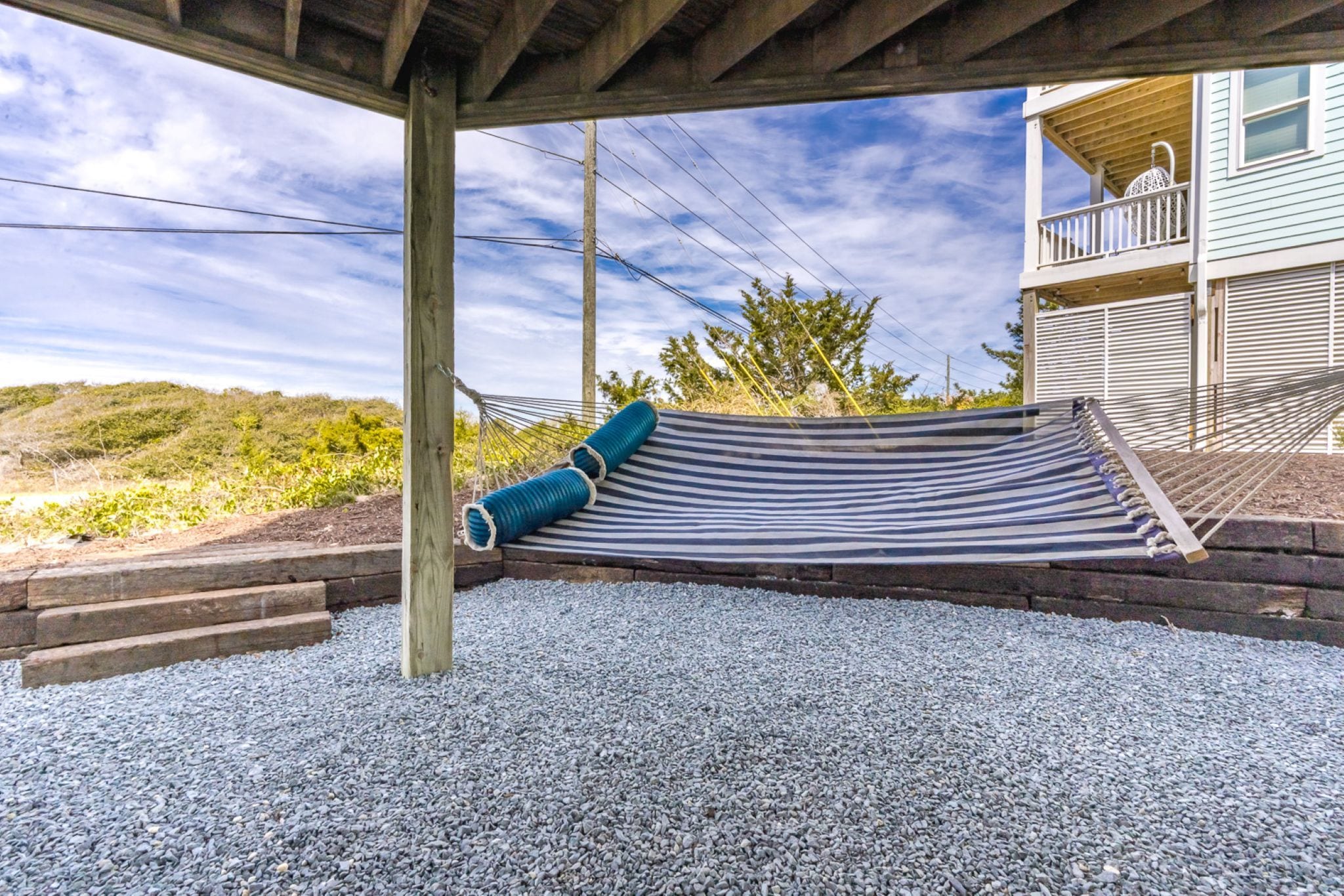A hammock under a wooden structure with a view of a house and vegetation.