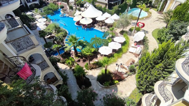 A rooftop pool area with multiple umbrellas, lounge chairs, and a small waterfall feature. - Luxuriöse Ferienwohnung im Harmony Suites Monte Carlo am Sonnenstrand (Sonnenstrand)