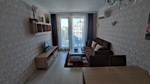 A modern living room with a sofa, coffee table, TV, and a balcony with a view. - Luxuriöse Ferienwohnung im Harmony Suites Monte Carlo am Sonnenstrand (Sonnenstrand)