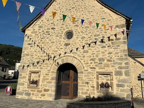 Un bâtiment en pierre avec une porte en bois, une fenêtre circulaire et un panneau indicateur avec des flèches directionnelles.