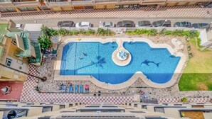 Vue aérienne d’un hôtel doté d’une grande piscine, de nombreux balcons et d’une zone dallée à motifs géométriques.