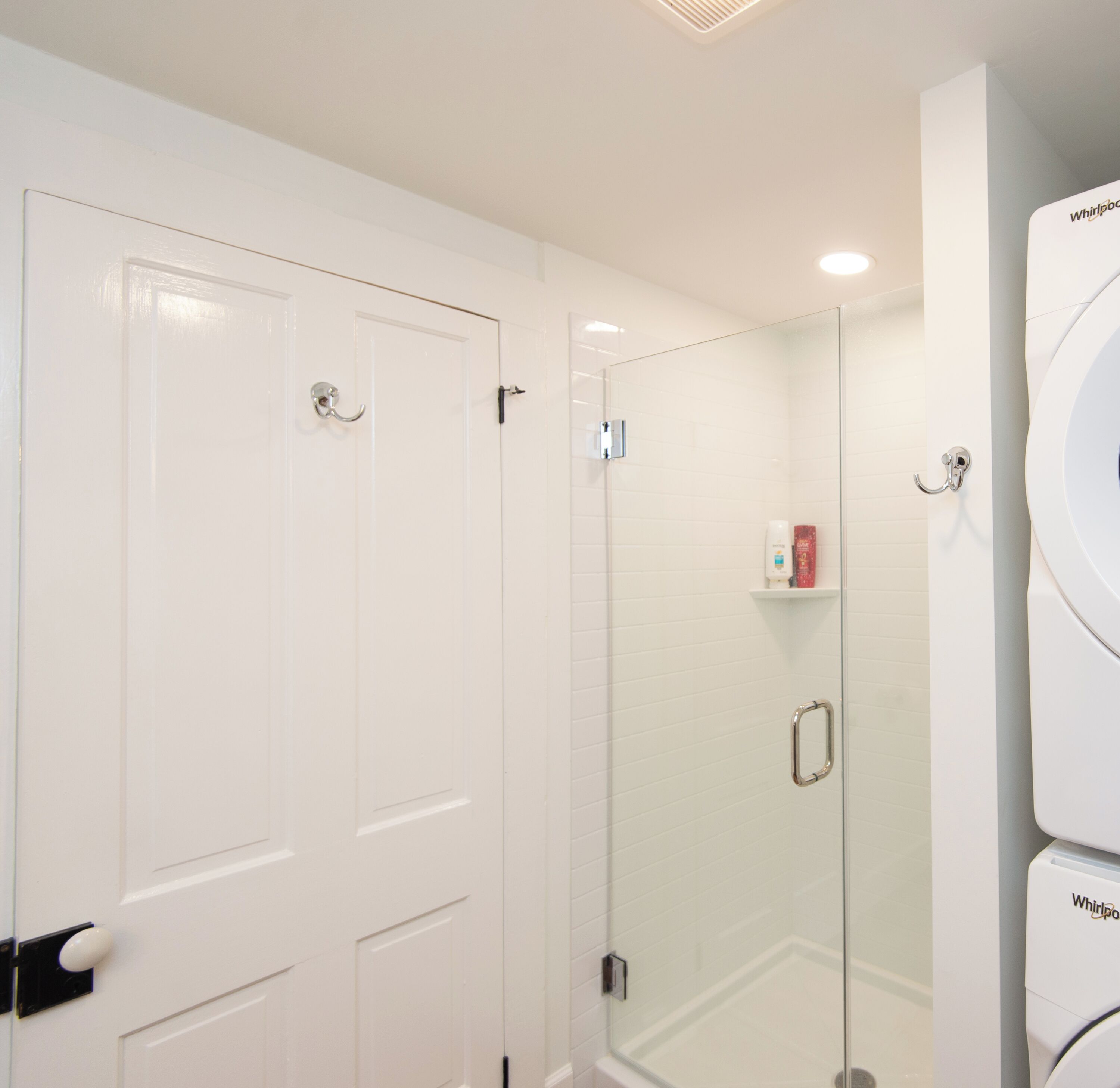 A bathroom with a white door, a glass shower enclosure, and a Whirlpool washing machine.