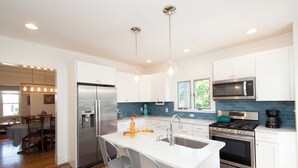 Uma cozinha moderna com armários brancos, eletrodomésticos de aço inoxidável e uma ilha central com banquetas.