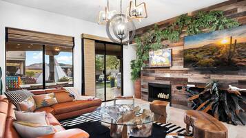 Una sala de estar moderna con sofás de cuero, una mesa de centro de vidrio, una chimenea y un ventanal con vistas a un jardín.