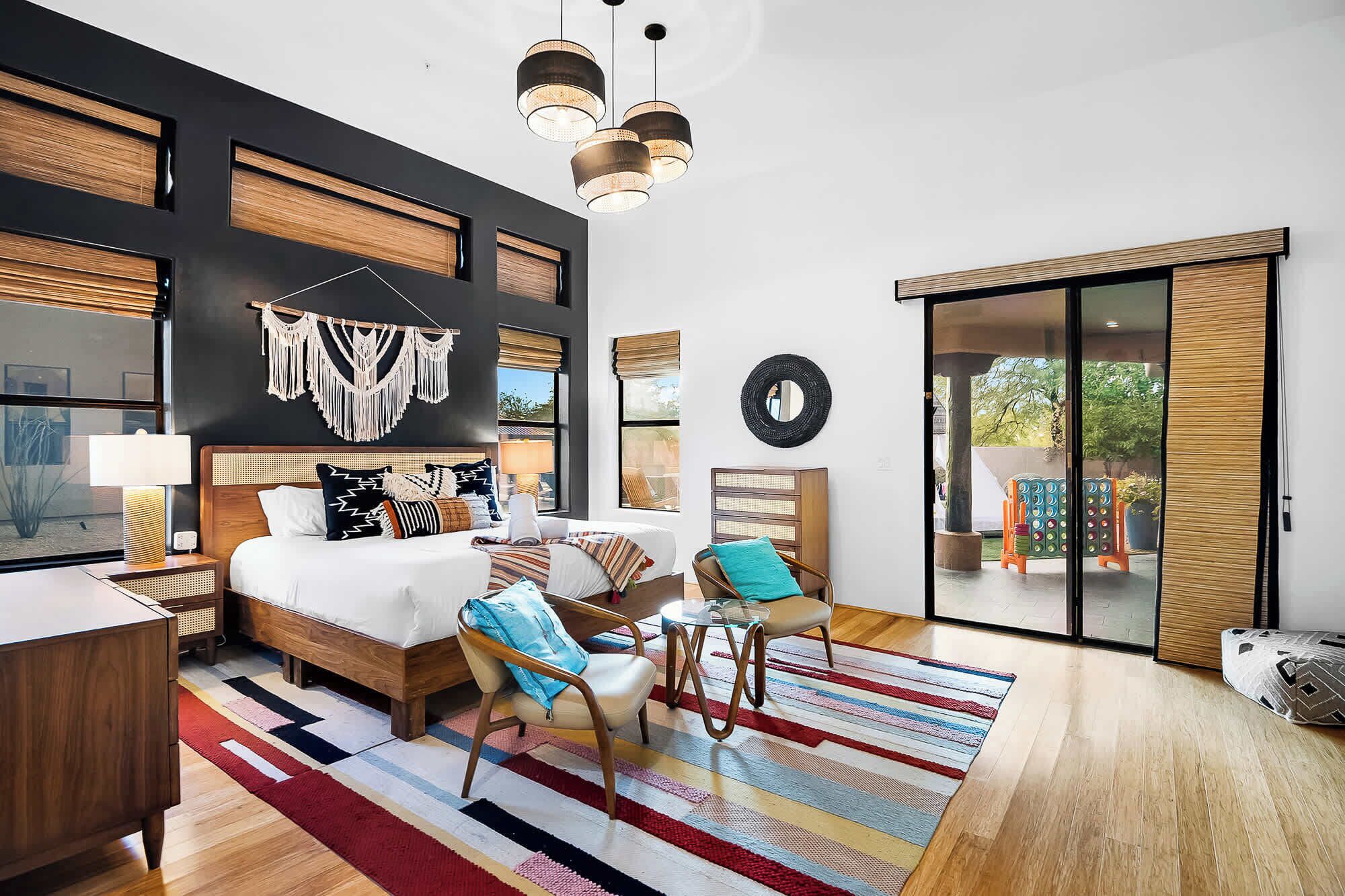 Habitación de hotel moderna con una cama grande, un escritorio, una silla, una alfombra colorida y vistas al exterior a través de una puerta corredera.
