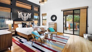 Une chambre d’hôtel moderne, dotée d’un grand lit, d’un bureau, d’une chaise, d’un tapis coloré et offrant une vue sur l’extérieur grâce à une porte coulissante.