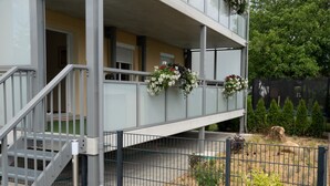 Een meerlaags gebouw met een balkon, een metalen trap en een omheinde tuin.