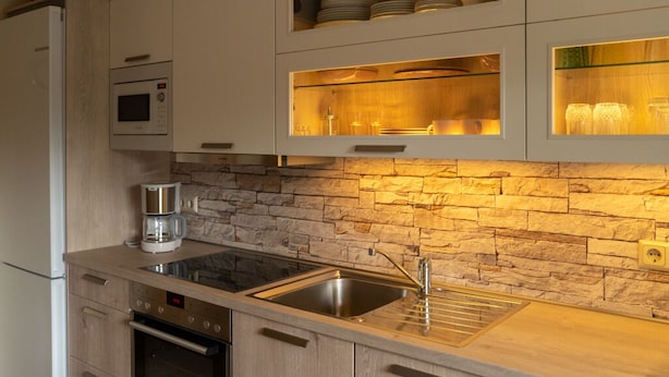 Een moderne keuken met een achterwand van steen, een ingebouwde magnetron en een RVS spoelbak.