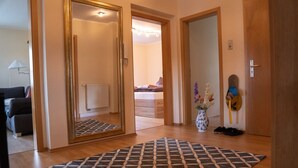 Een gang met een kamerbreed tapijt, een spiegel, een vaas met bloemen en een deur naar een slaapkamer.