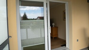 Een kamer met een schuifglasdeur naar een balkon, een houten kastje en een lijst met een afbeelding aan de muur.