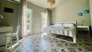 A hotel room with a bed, bedside table, desk, chair, and a large window with curtains.