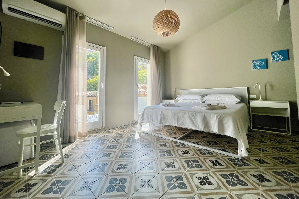 Une chambre d’hôtel comprenant un lit, une table de chevet, un bureau, une chaise et une grande fenêtre avec des rideaux.