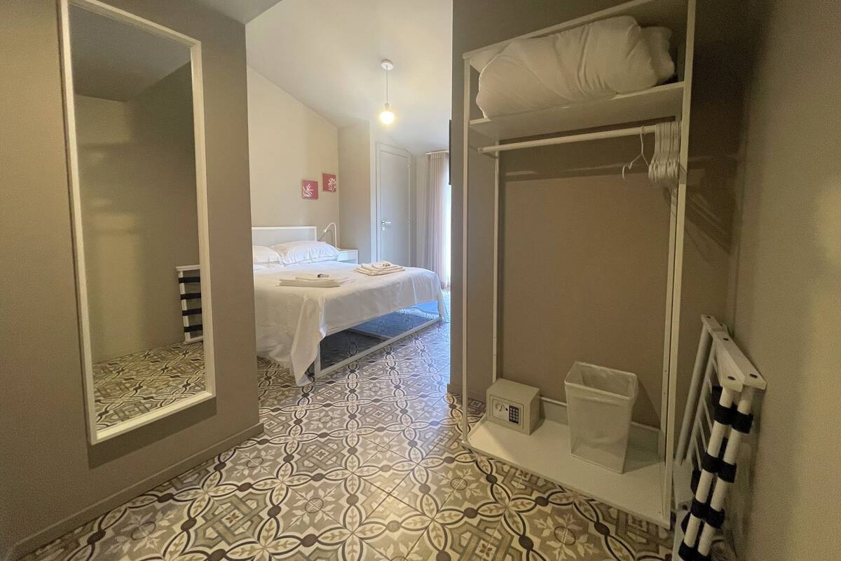 Une chambre d’hôtel avec un lit, un miroir, une armoire et une petite table de chevet avec une lampe.