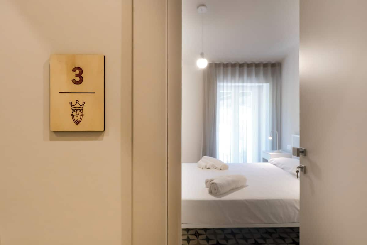 Une chambre d’hôtel avec un lit, une table de chevet, une lampe et une fenêtre avec des rideaux.