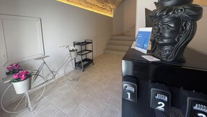 A reception area with a stone ceiling, a reception desk with a bust sculpture, a bicycle with flower baskets, and a staircase in the background.