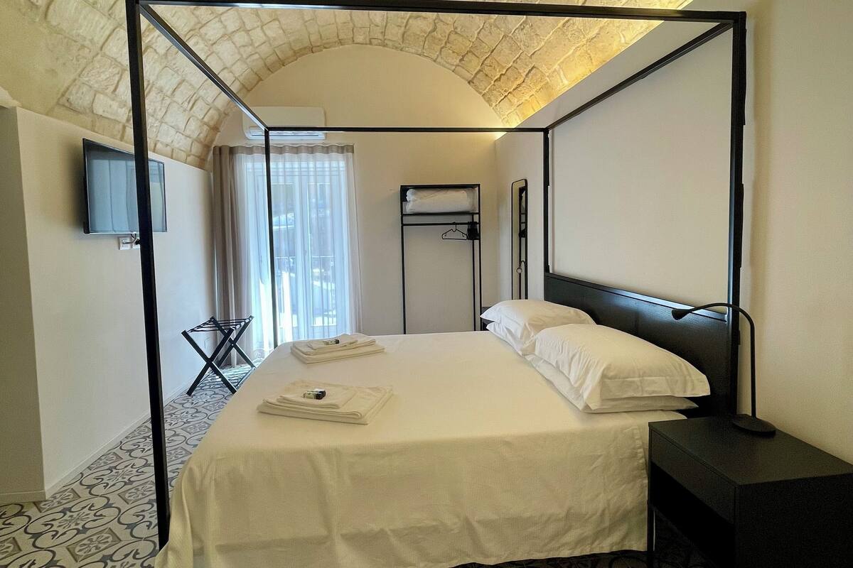 Une chambre dotée d’un lit à baldaquin, d’un téléviseur à écran plat fixé au mur, d’une petite table et d’un sol à motifs.