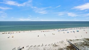 A wide sandy beach with umbrellas and beach chairs, a clear blue sky, and the ocean in the background.